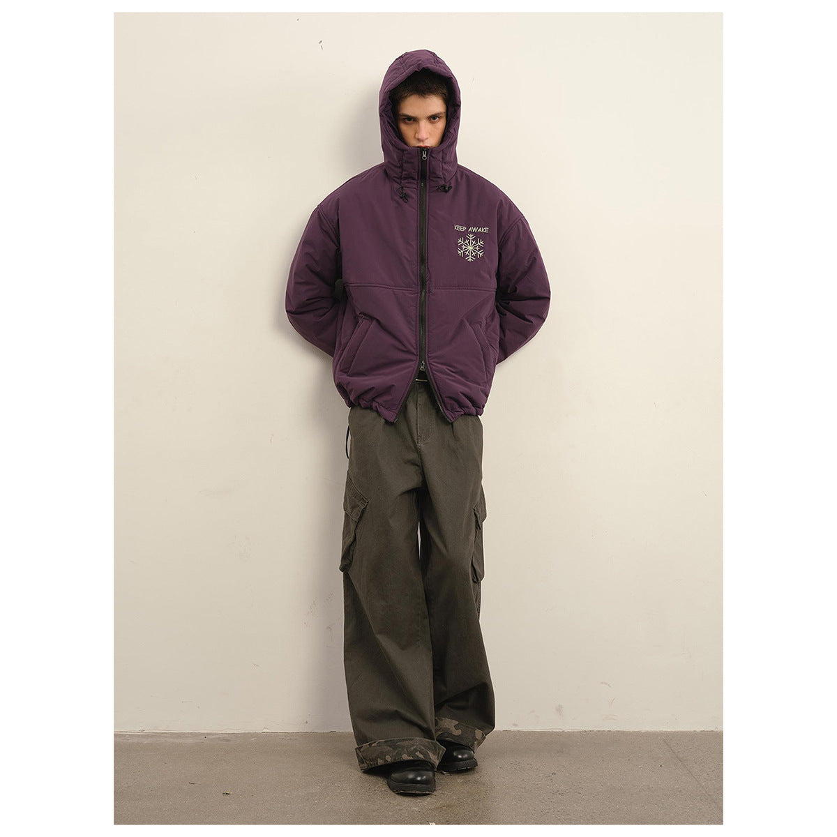 Front view of a model in a plum hooded jacket zipped high, with light snowflake embroidery and dark cargo pants.