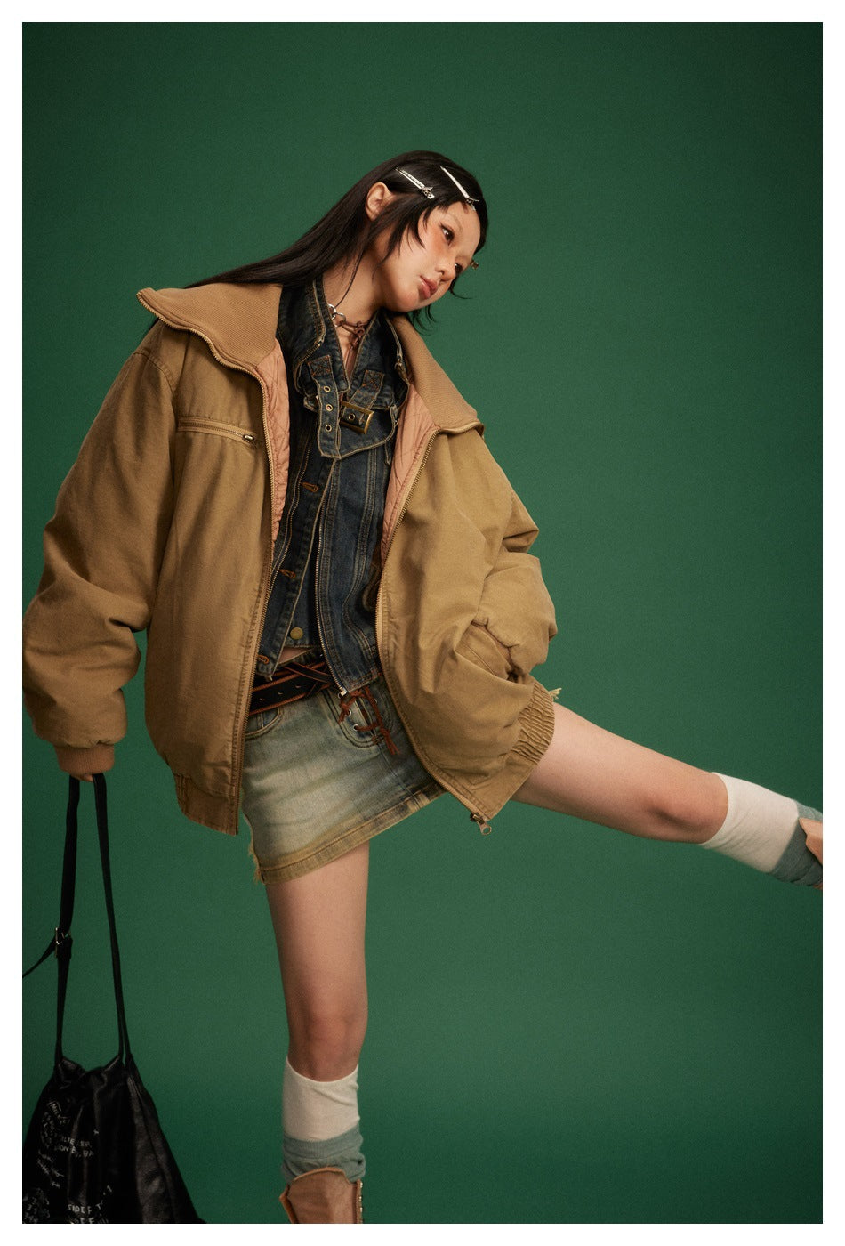 Model wearing an open tan zip jacket over a denim vest and denim mini skirt.