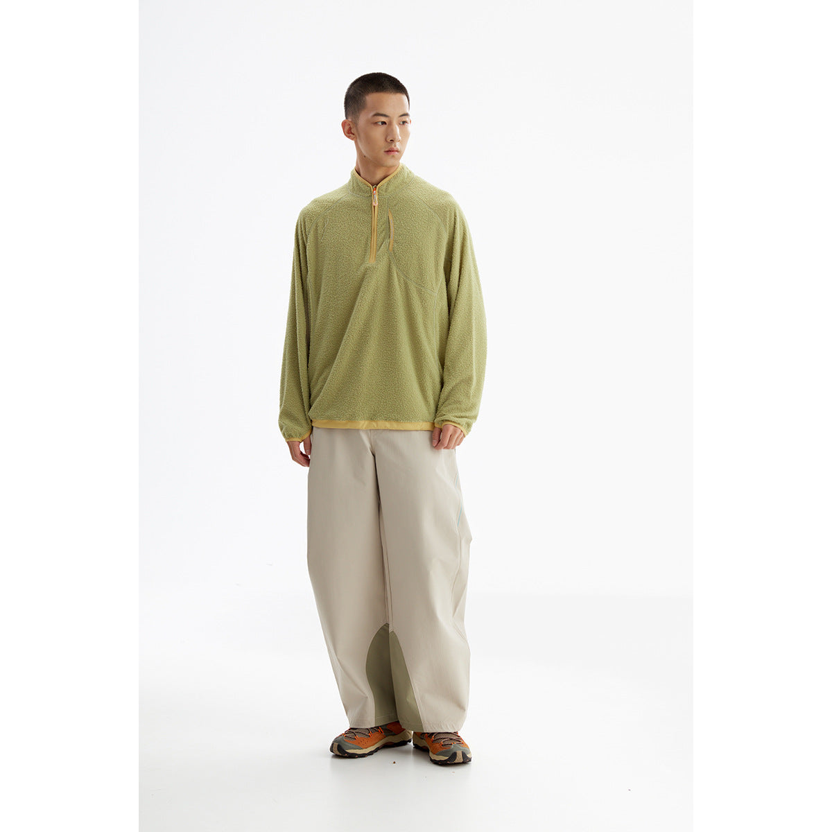 Full-length model wearing an olive quarter-zip fleece with yellow trim and loose light beige trousers.