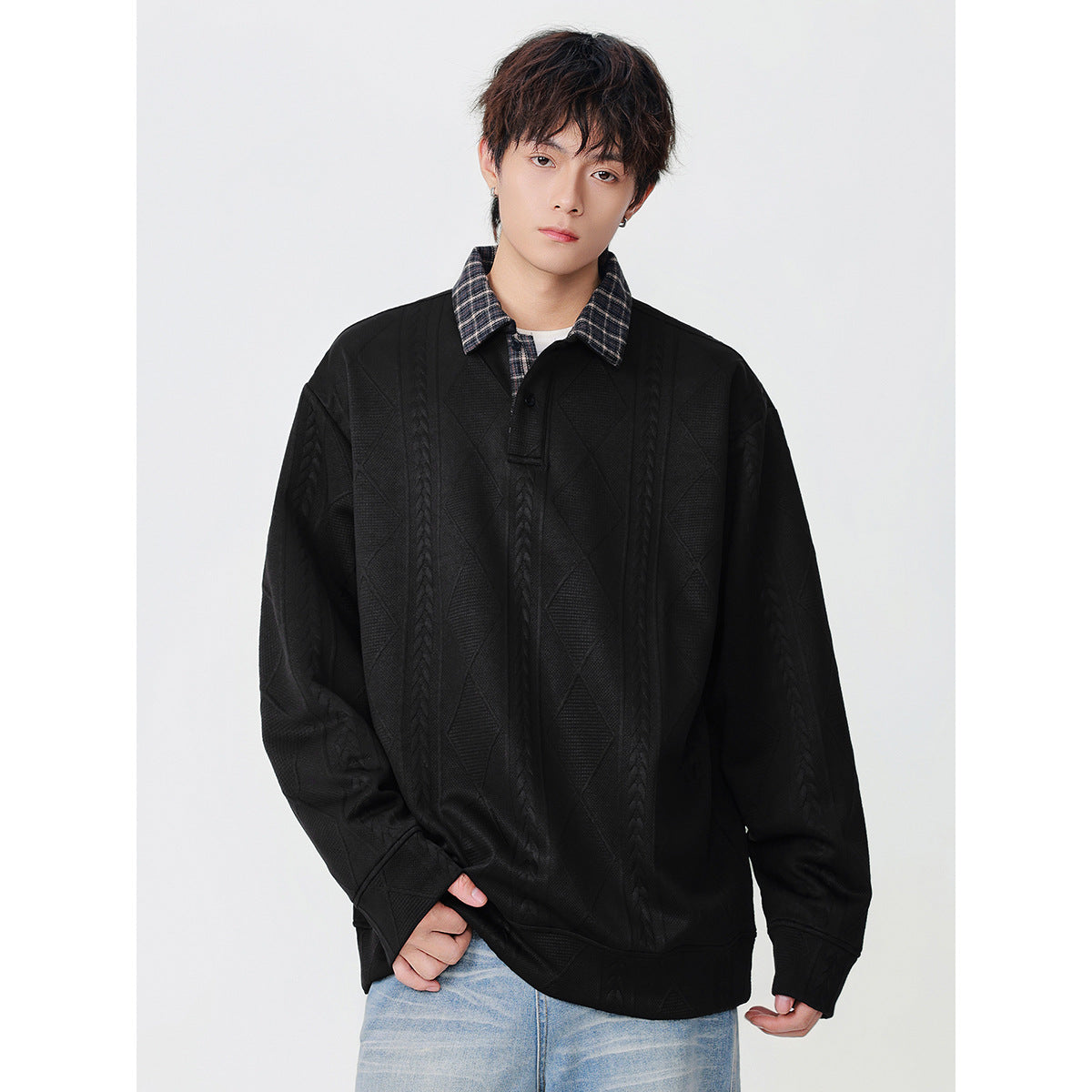 Front view of a model wearing a black oversized pullover with a plaid collar and raised cable and diamond patterns.