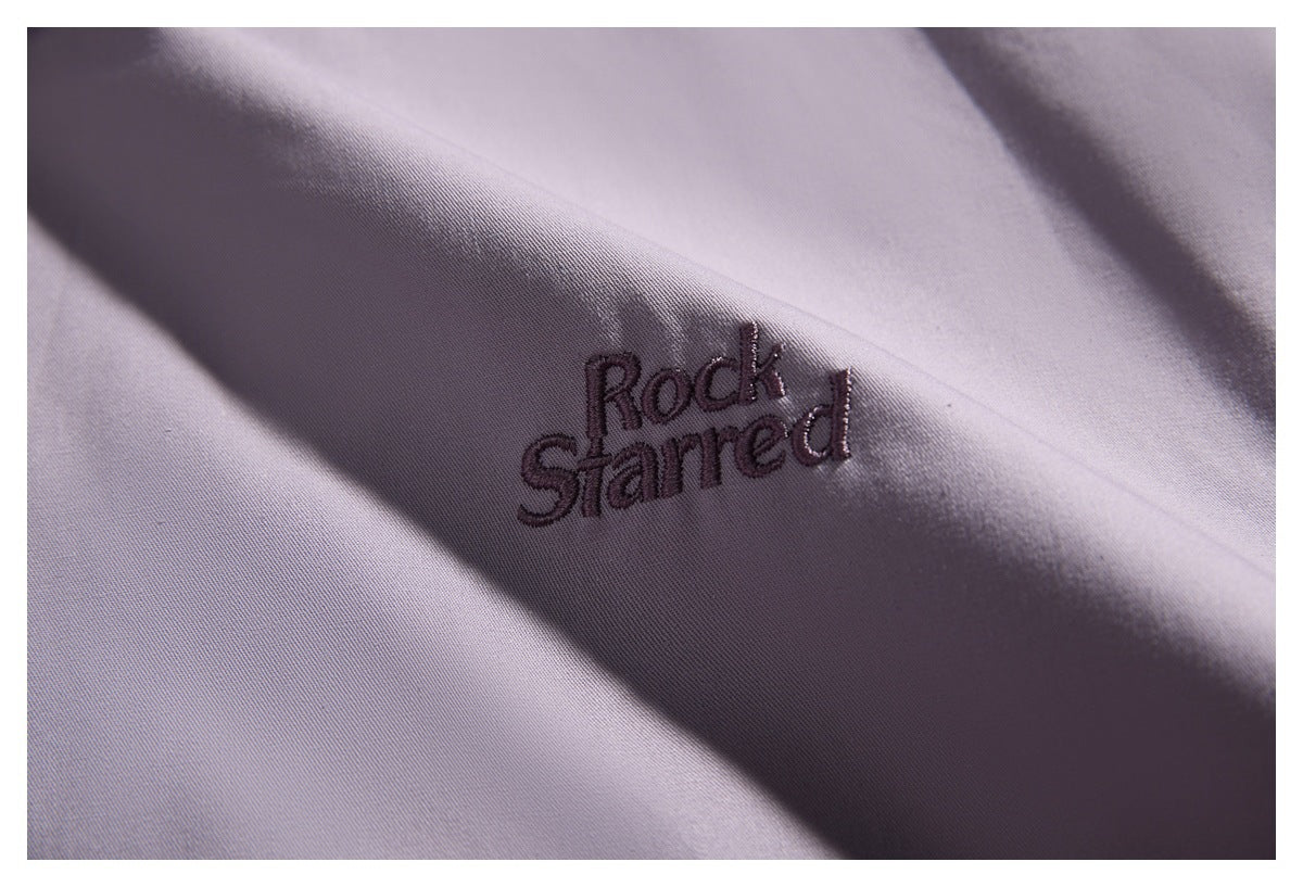 Close-up of dark “Rock Starred” embroidery on lavender fabric, shown across a fold.