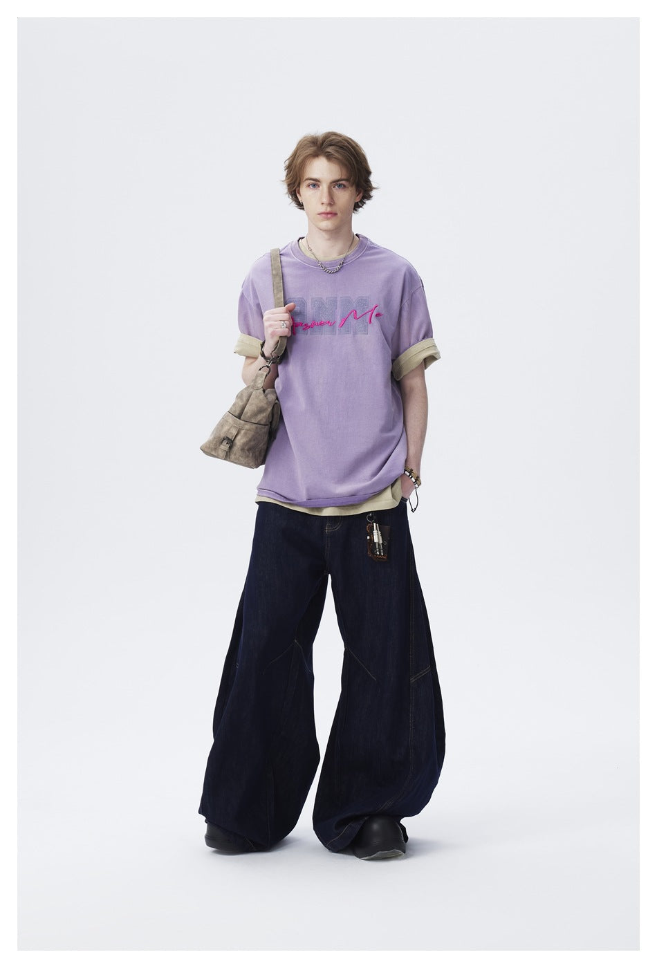 Model wearing a lavender graphic T-shirt with rolled sleeves and very wide dark jeans.