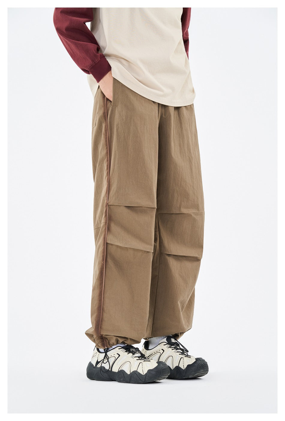 Model wearing khaki wide-leg pants with side piping, pleated knees and a drawstring hem, with a cream top and sneakers
