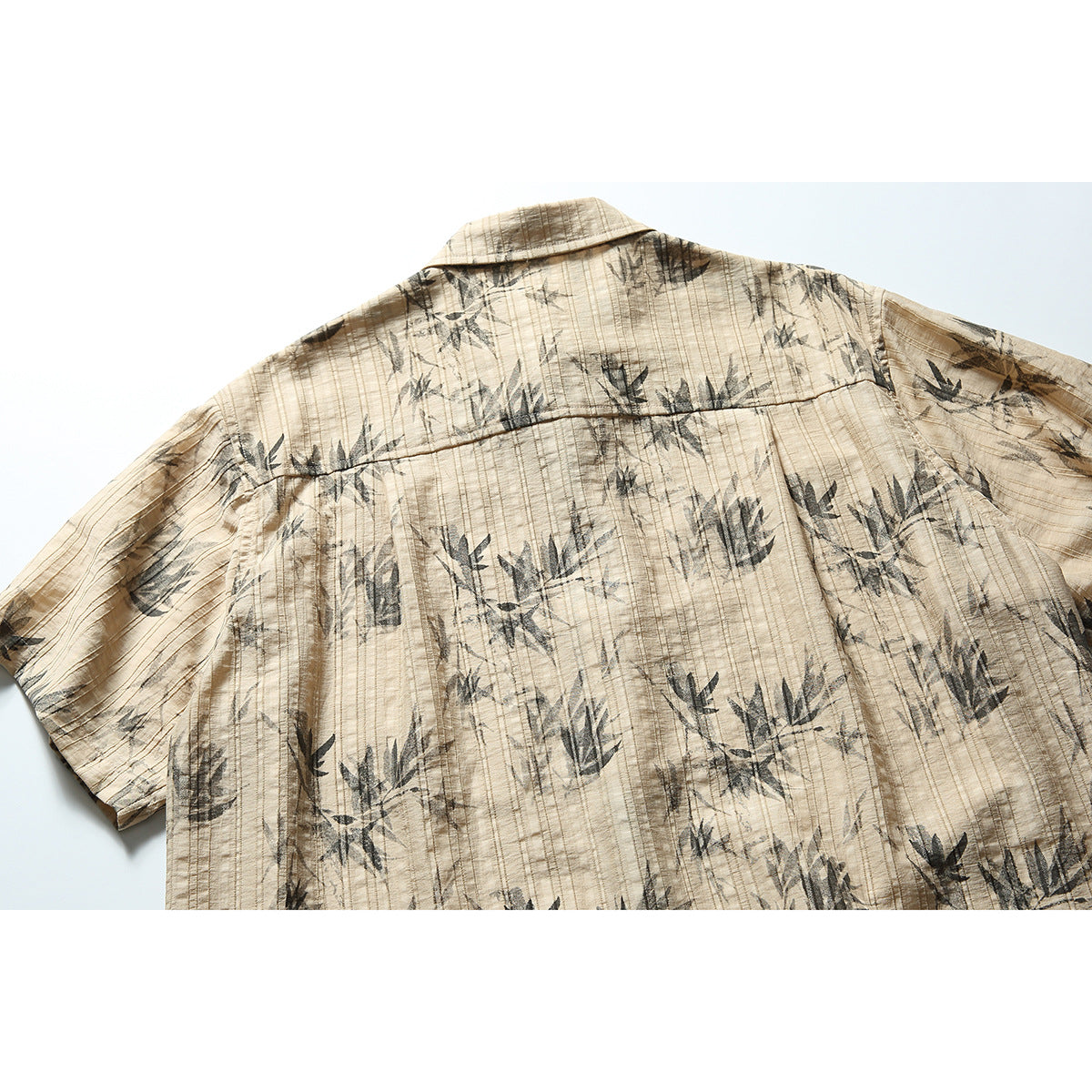 Back view of a tan short-sleeve shirt with a dark botanical print, back yoke, and vertical stitching.