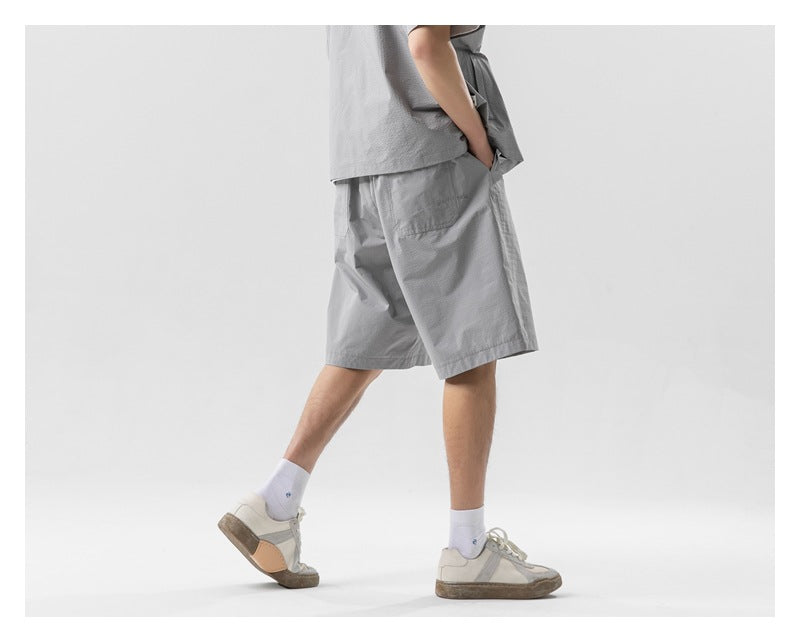 Side-rear view of a model wearing light gray knee-length shorts with a matching shirt.