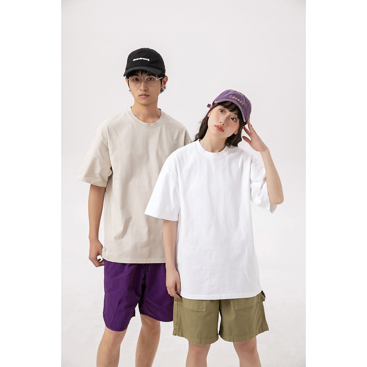Two models wearing oversized short-sleeve T-shirts in cream and white, with casual shorts and caps.