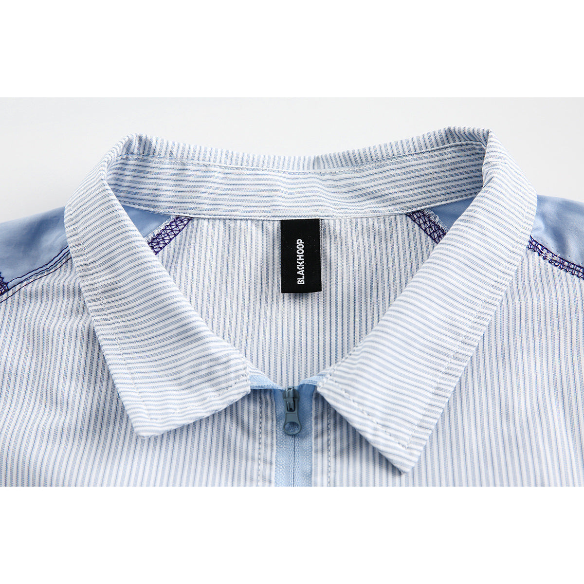Close-up of a light blue and white striped shirt collar, zipper, and BLACKHOOP neck label.