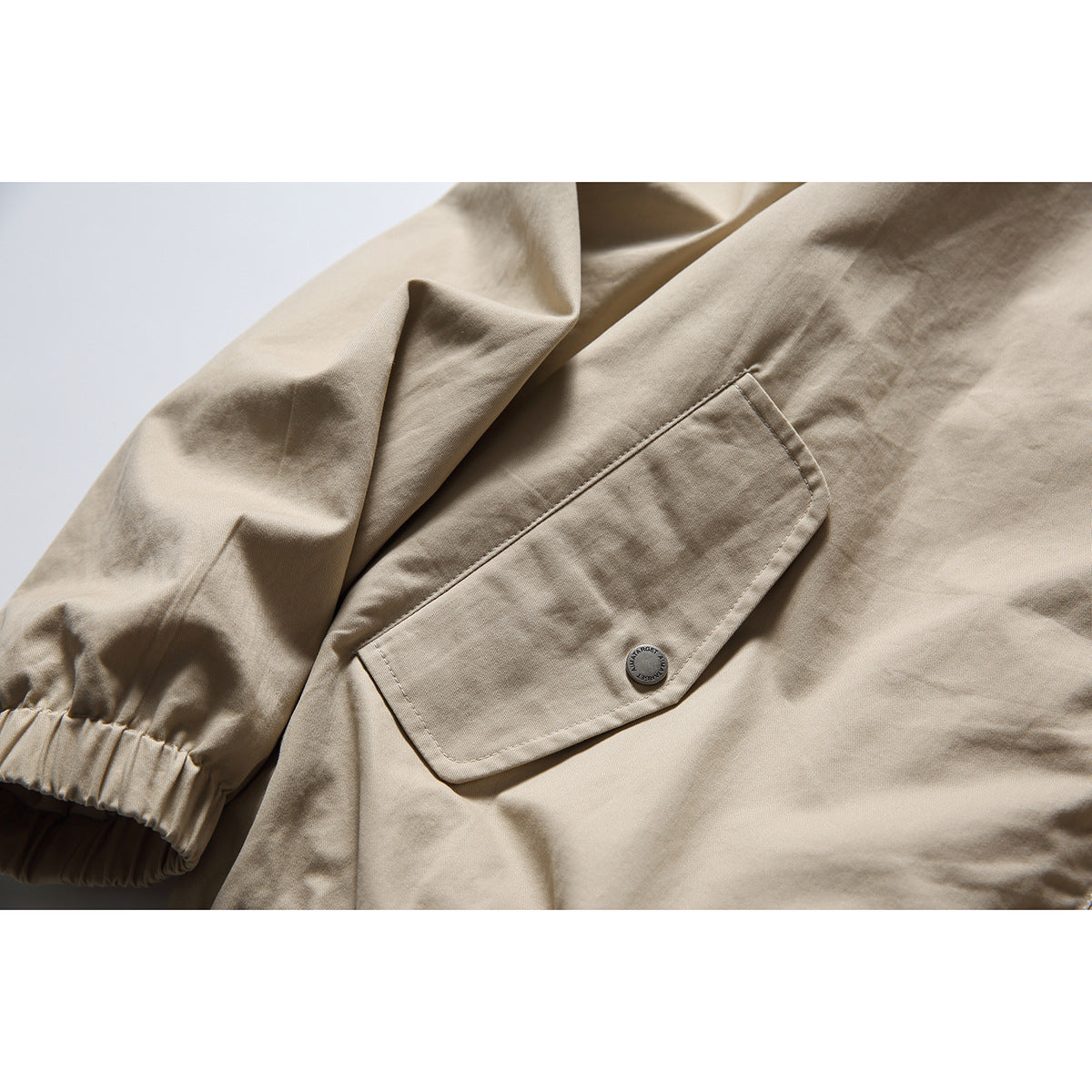 Close-up of the beige jacket’s flap pocket, button, stitching, and gathered sleeve cuff.