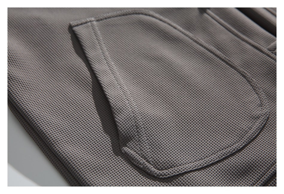 Close-up of a stitched pocket on dark gray, finely textured garment fabric.