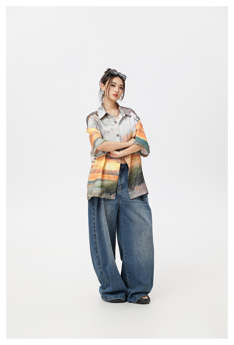 Three-quarter front view of a model wearing a multicolored printed short-sleeve button-up shirt and wide-leg jeans.