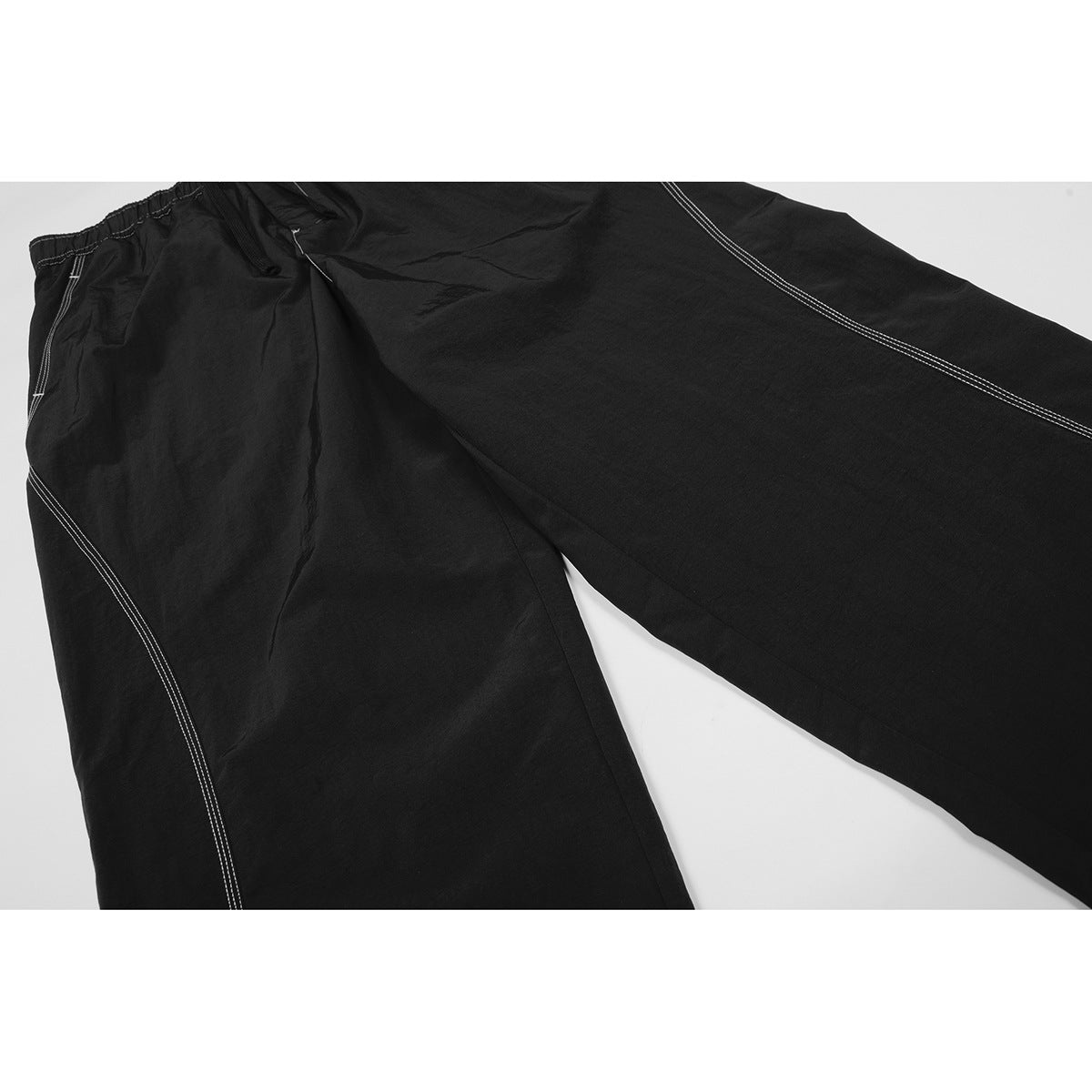 Close-up of black wide-leg pants showing the waistband, pockets, and white contrast stitching.