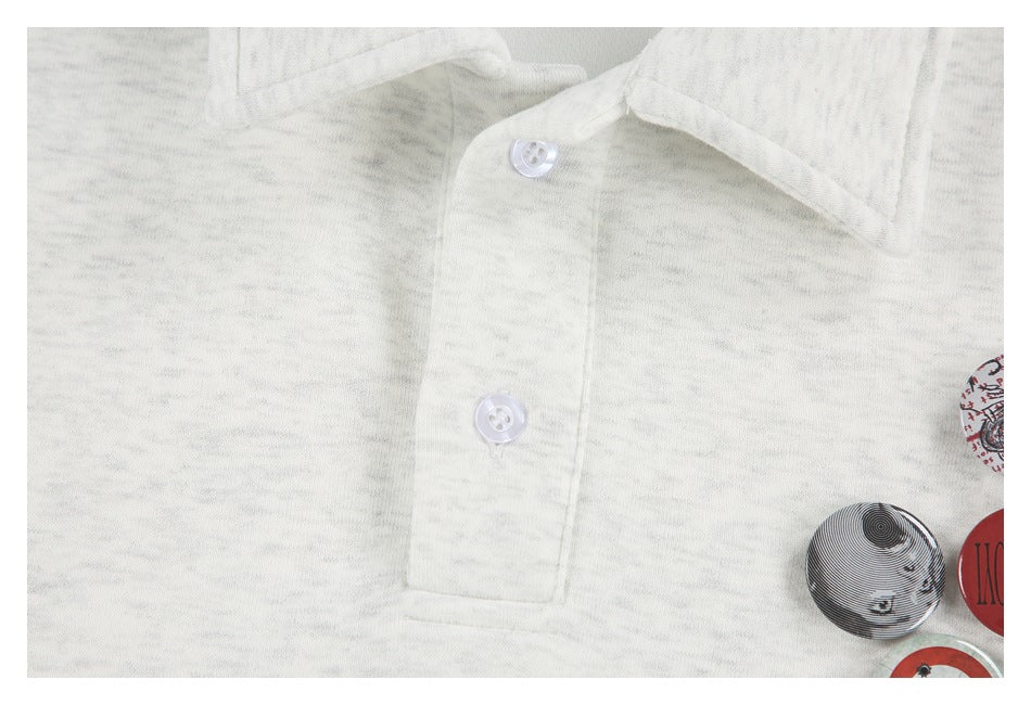 Close-up of the pointed collar, two white buttons, and graphic badges on a light gray marled pullover.