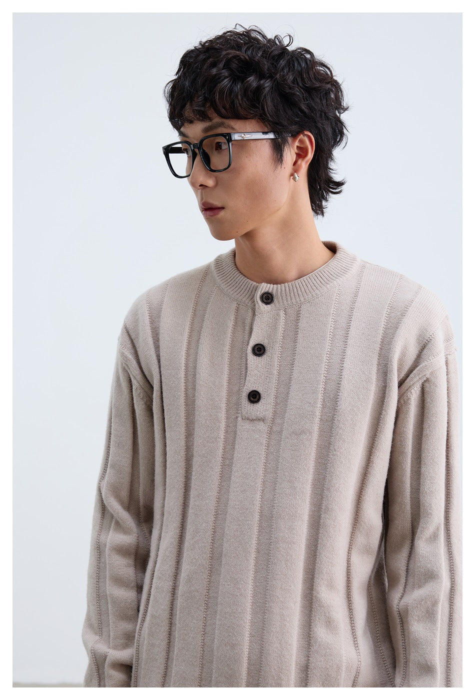 Close-up of a model wearing a pale beige sweater with vertical ribbed panels and a three-button neck.