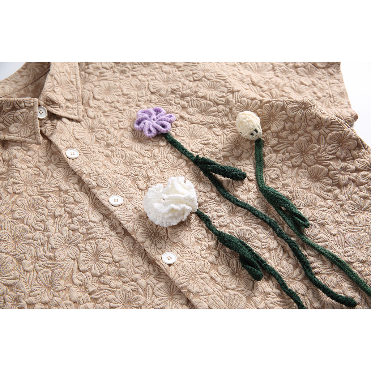 Close-up of the beige shirt's raised floral texture, white buttons and purple and white flower appliqués with green stems.