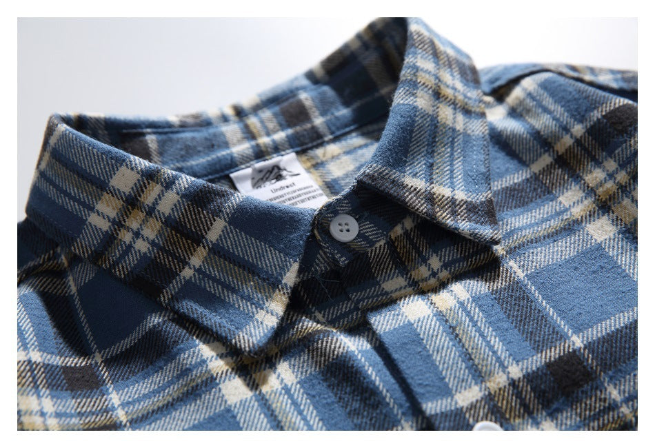 Close-up of the pointed collar and top button on a blue, navy, and cream plaid shirt.