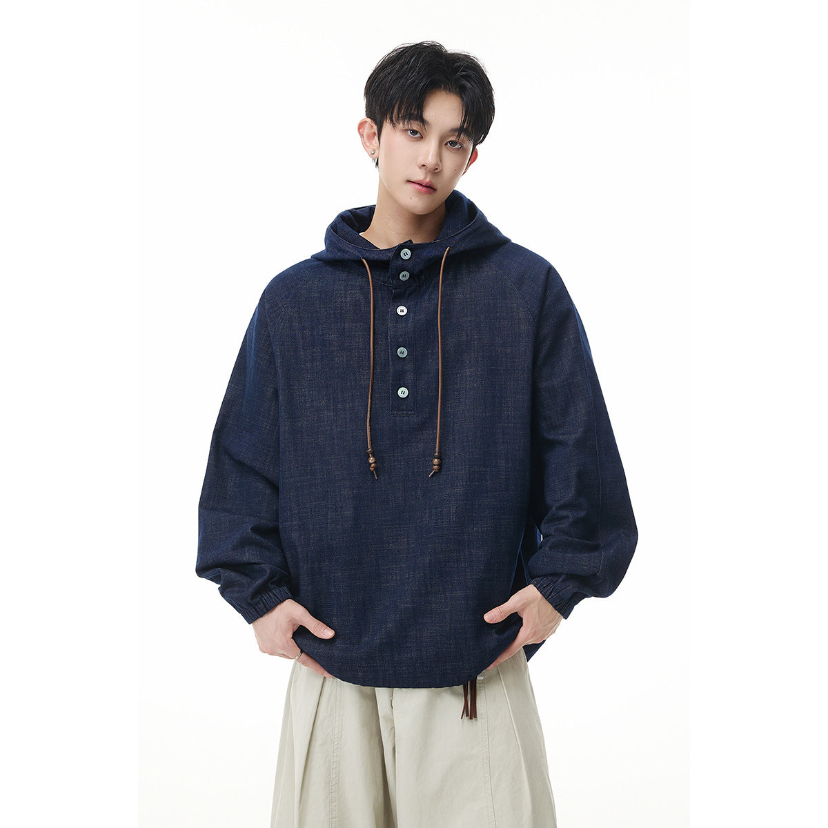 Model wearing a dark navy hooded pullover with a button placket, long brown drawcords, and cream wide-leg trousers.