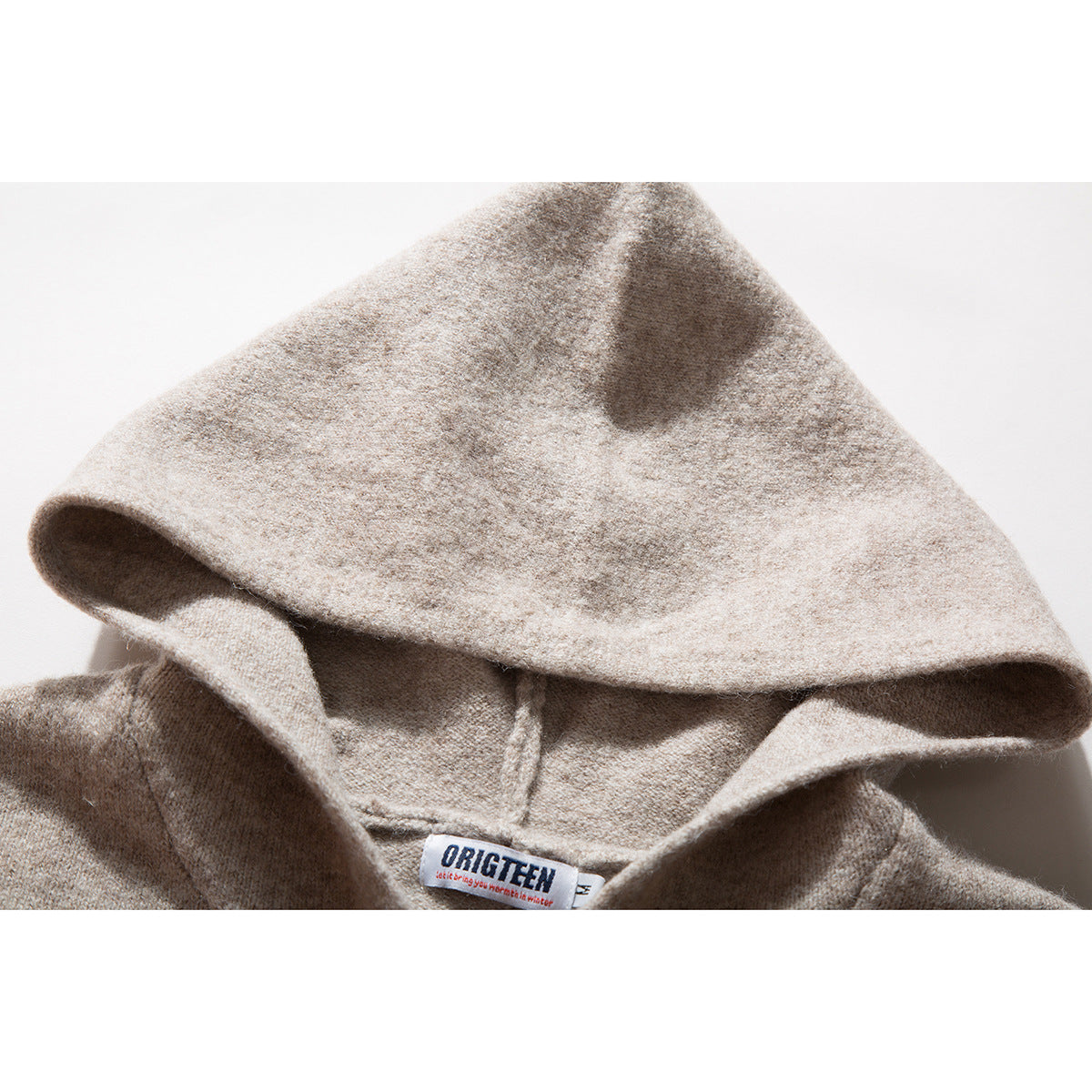 Close-up of a beige knit hoodie hood and neckline, showing the sewn neck label.