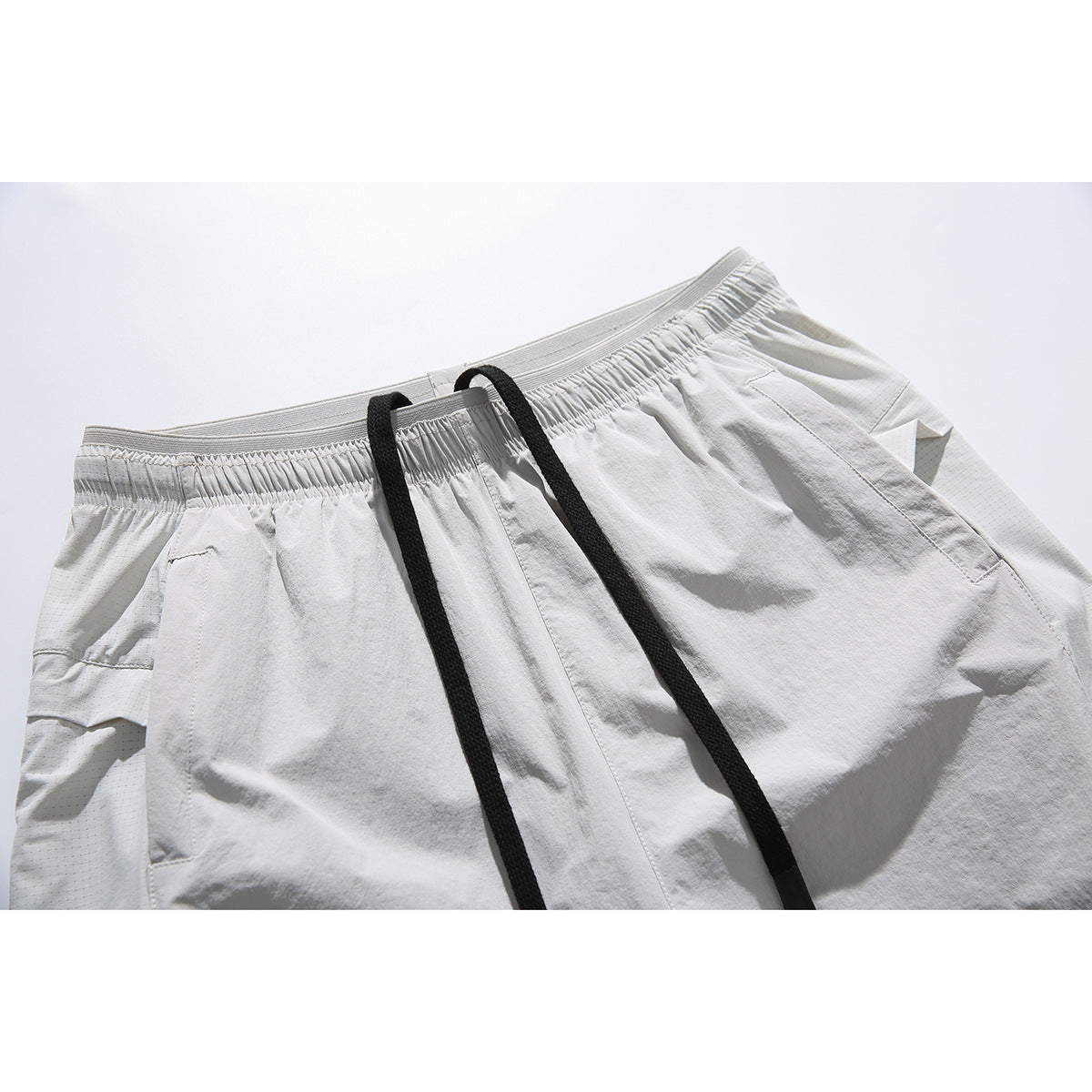Close-up of white shorts with an elastic waistband, long black drawstrings, and angled side pockets.