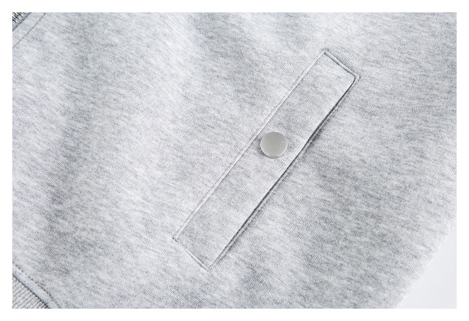 Close-up of a rectangular flap pocket with a metal snap on the light gray hoodie.