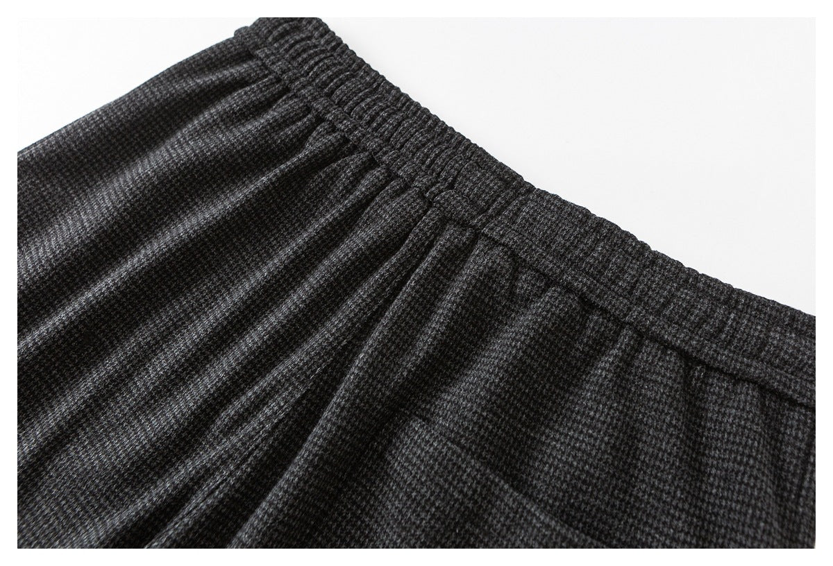 Close-up of trousers with an elasticized waistband and gathered pleats in a dark gray pattern.