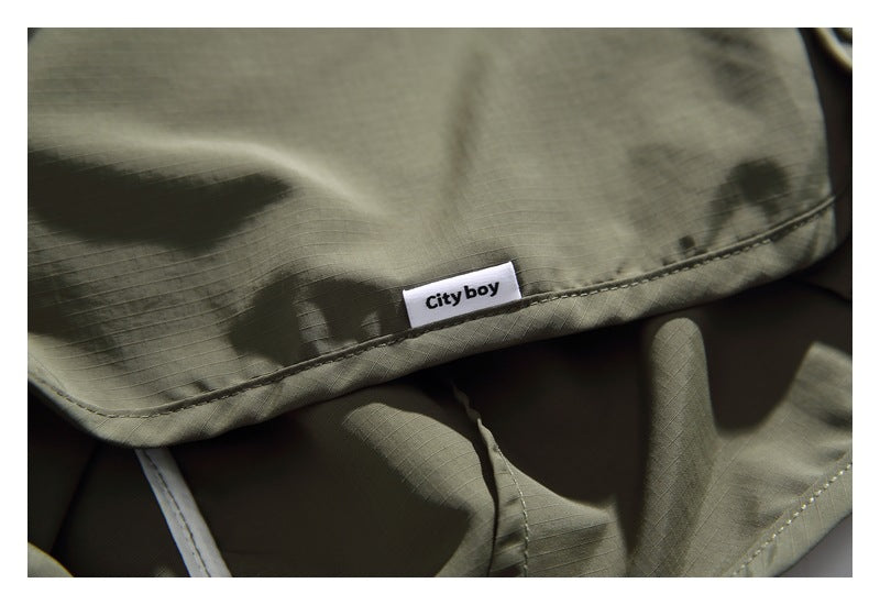 Close-up of olive-gray garment fabric and stitching with a small sewn-in “City boy” label.