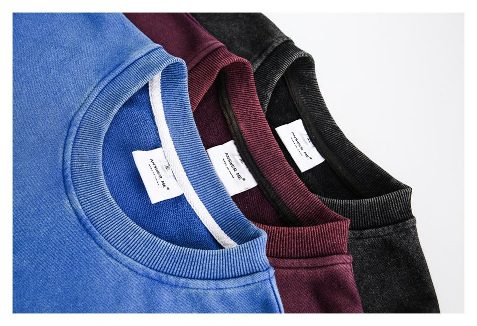 Close-up of blue, burgundy, and charcoal crewneck sweatshirts showing ribbed collars and interior labels.