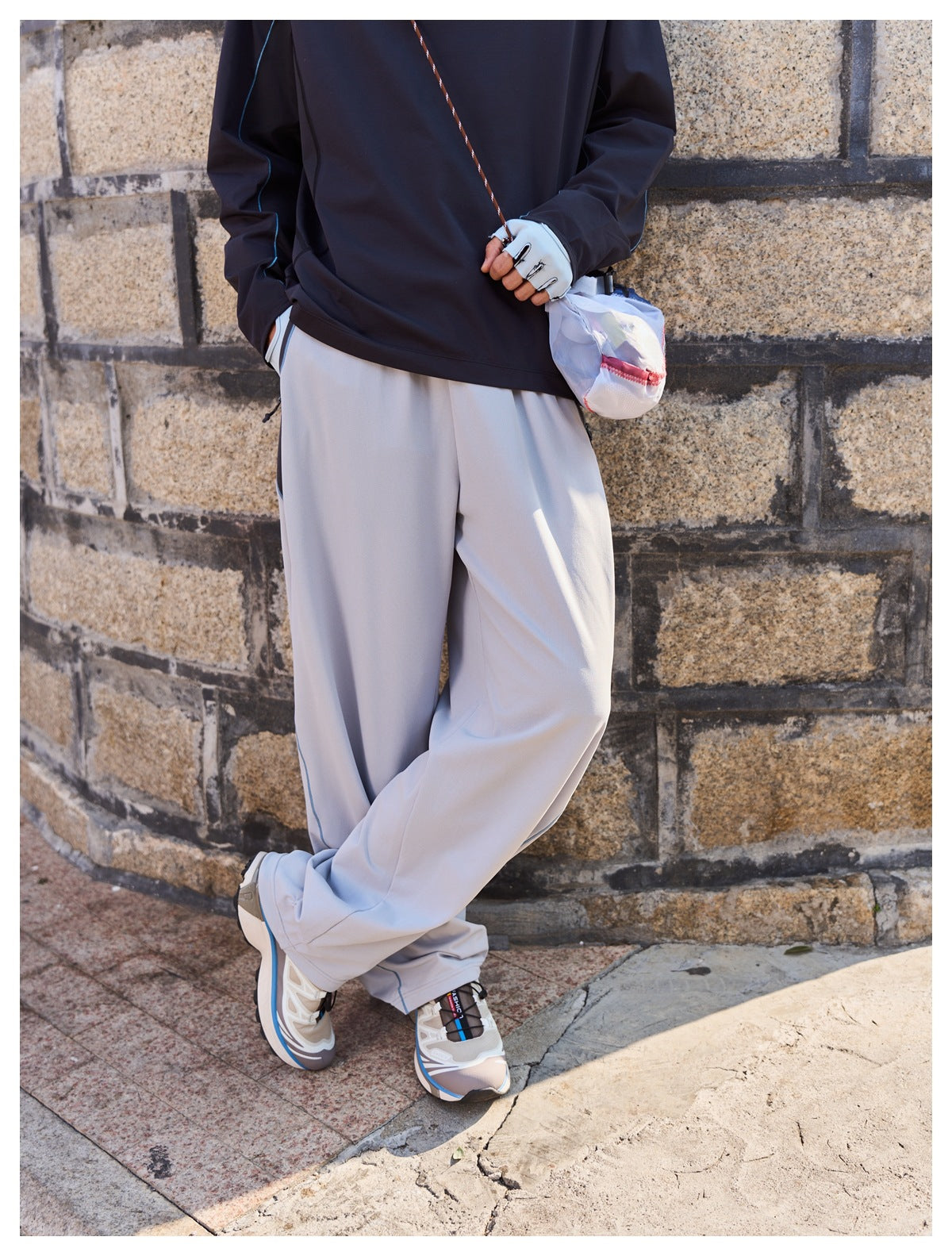 Close view of loose light-gray trousers with blue piping, shown from the front with part of a dark top.