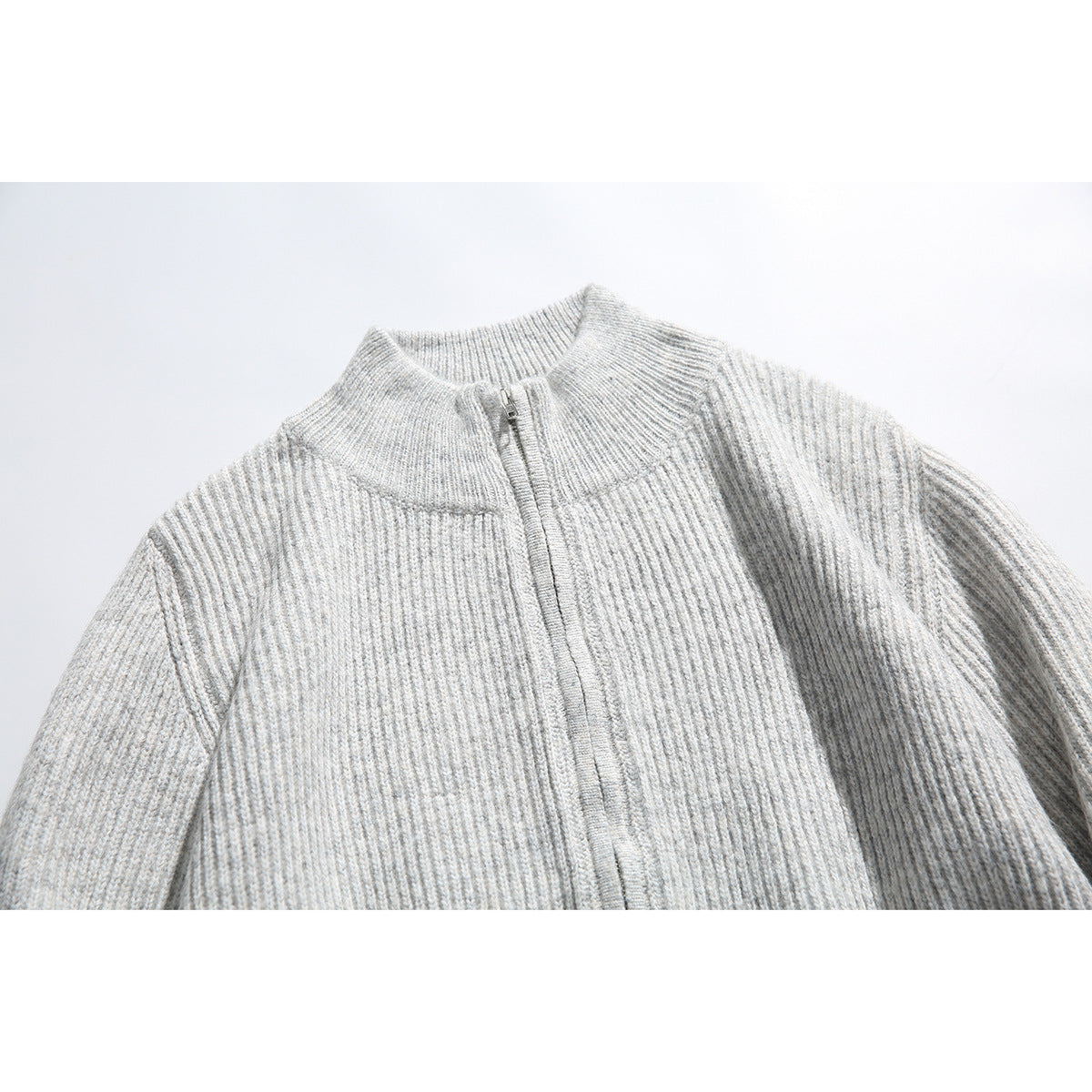 Close-up of a light gray rib-knit zip sweater showing its stand collar and front zipper.