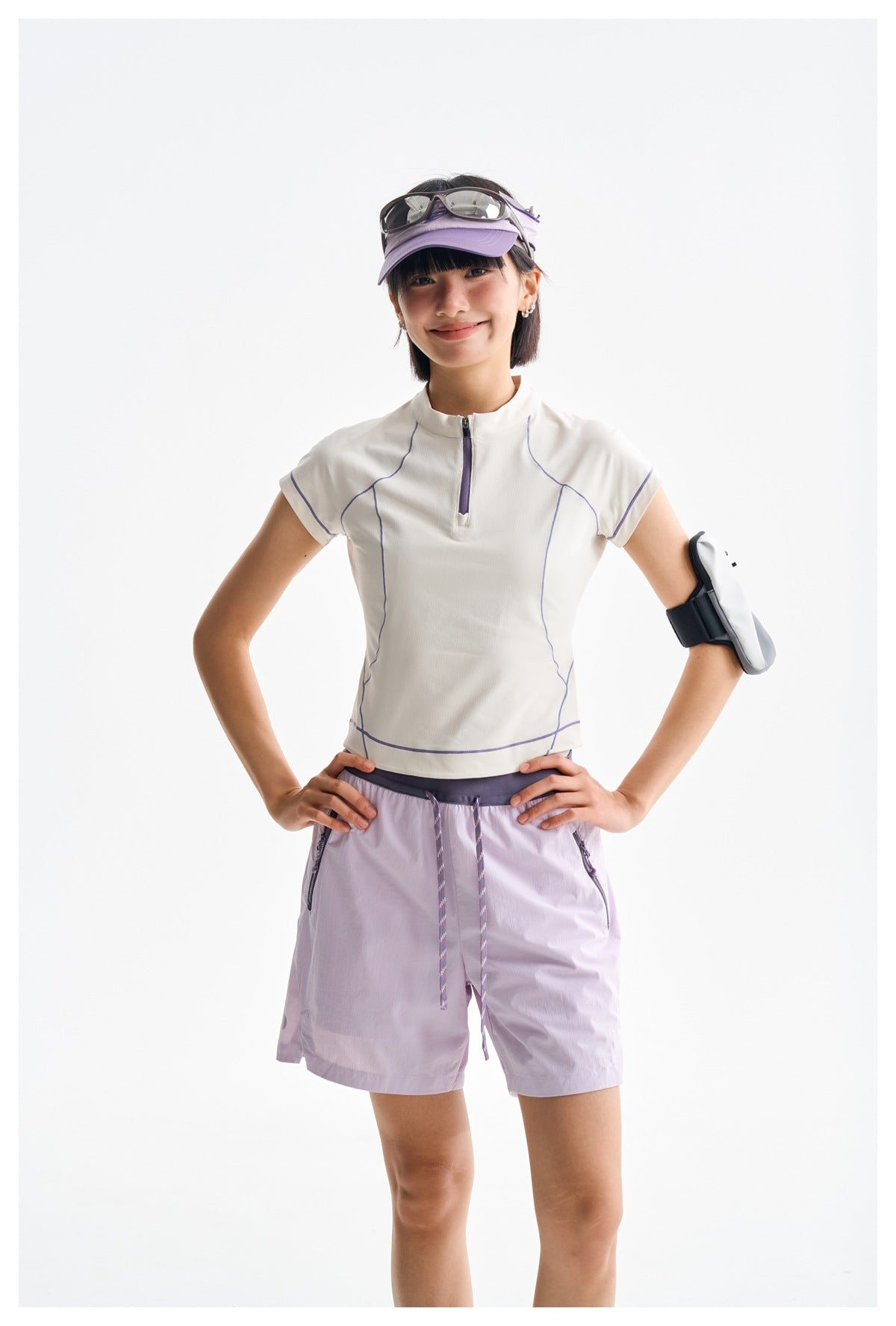 Model wearing a white zip-neck top with purple piping and lavender shorts with drawstrings and zip pockets.