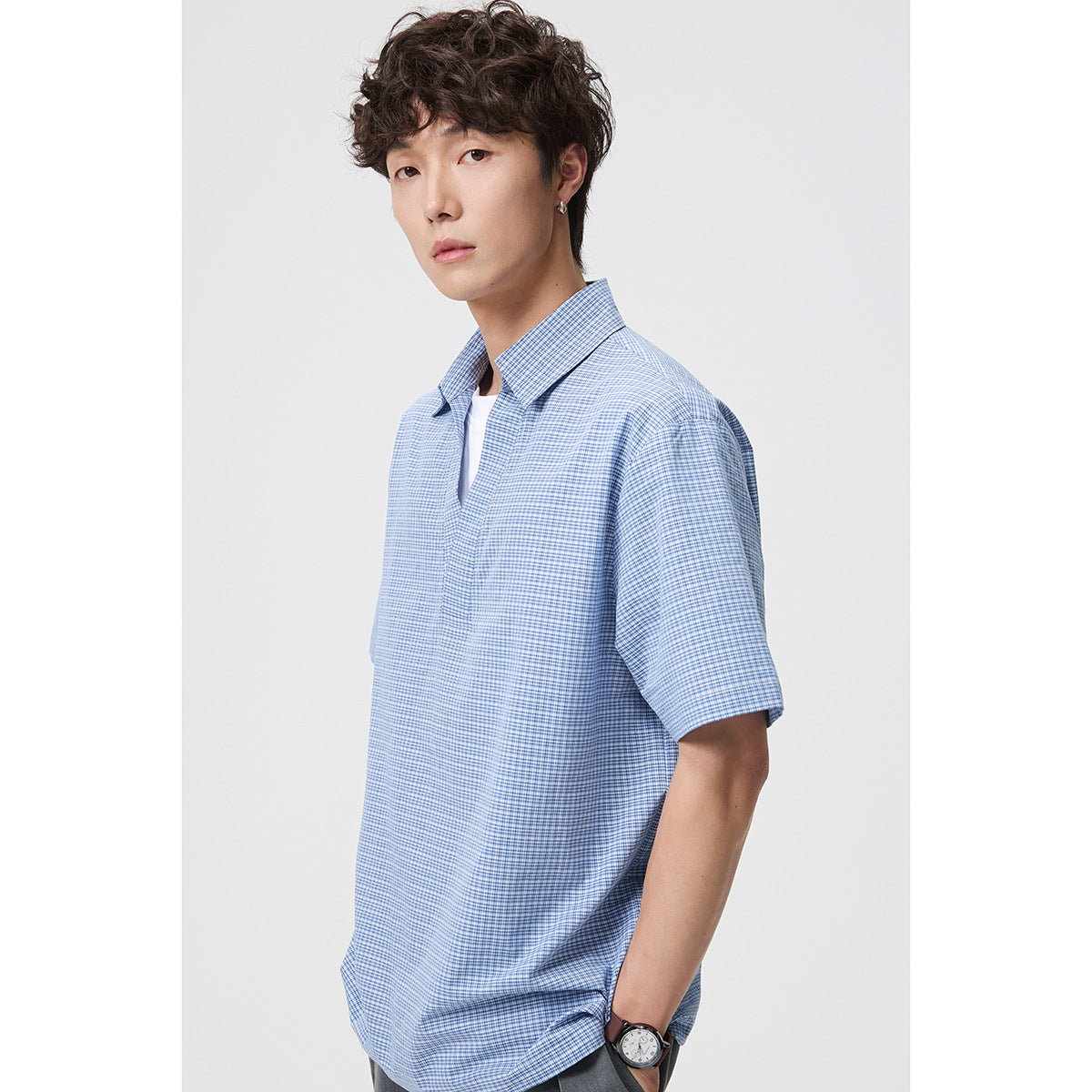 Man modeling a blue-and-white micro-check short-sleeve collared shirt with an open V-neck placket.