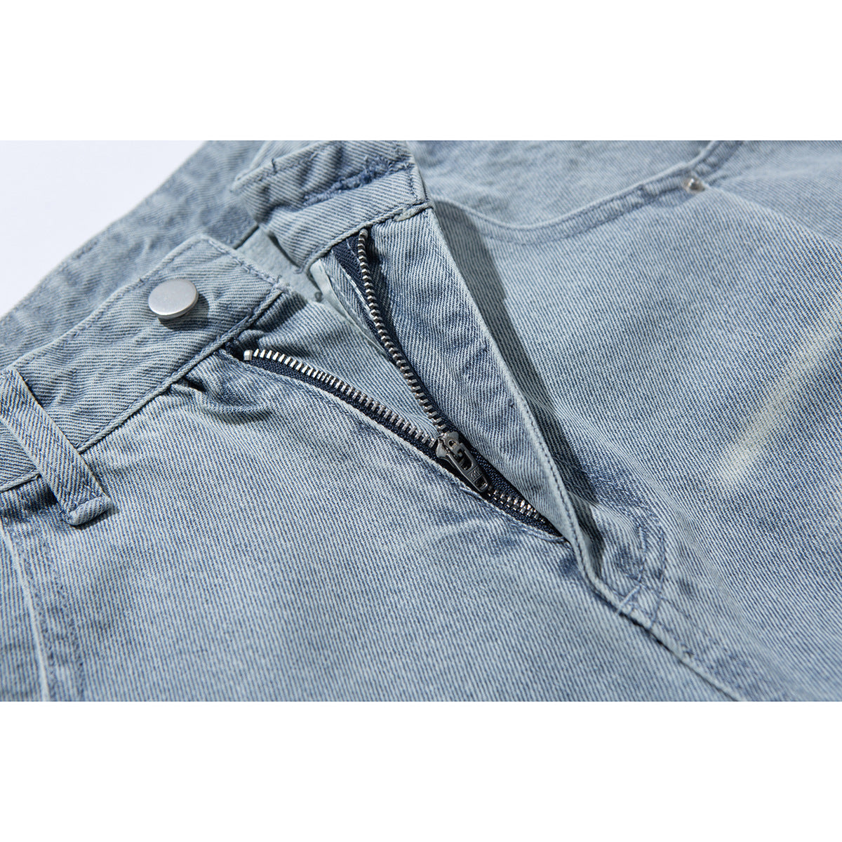 Close-up of light-wash jeans with the fly unzipped, showing the zipper, button and stitching.