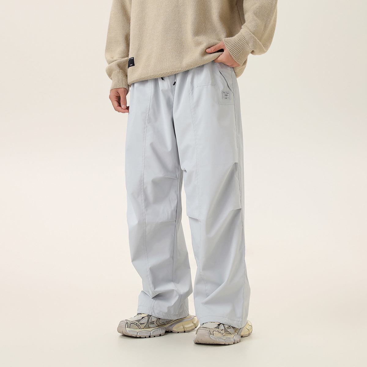 Model wearing light gray, wide-leg pants with a drawstring waist, panel seams, and a small thigh patch, front view.