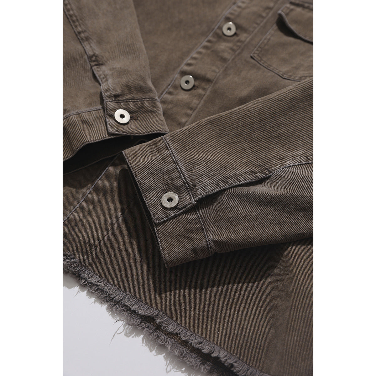 Close-up of the brown shirt's buttoned sleeve cuff and frayed hem, with part of the front pocket visible.