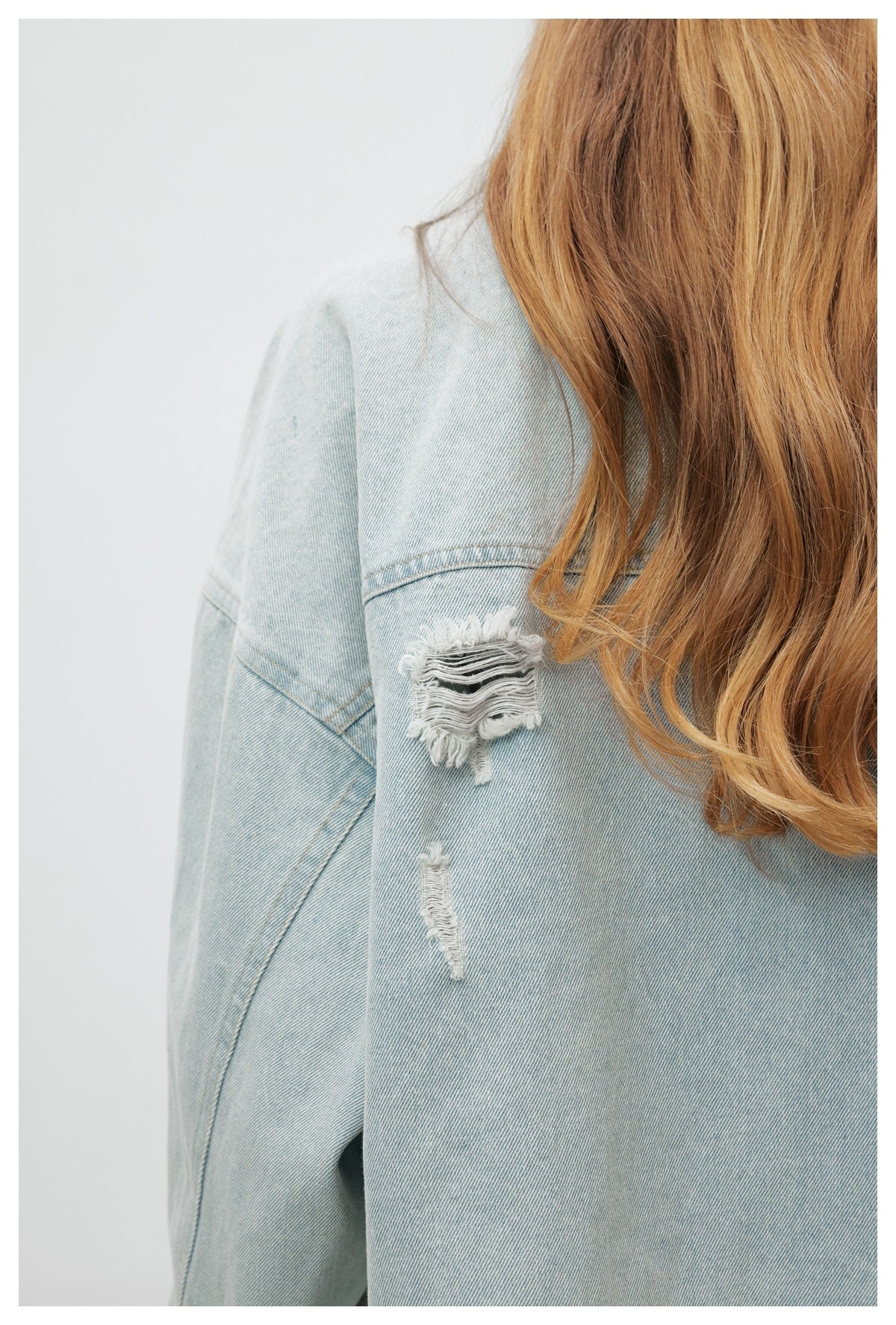 Close-up of frayed distressed patches on the sleeve of a light-wash denim jacket.
