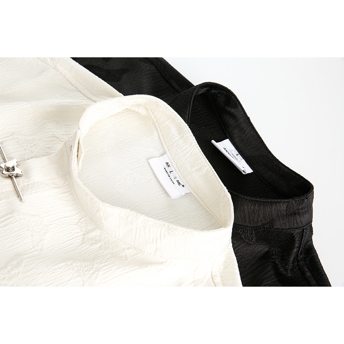 Close-up of white and black stand collars with sewn-in labels and a silver decorative closure on the white shirt.