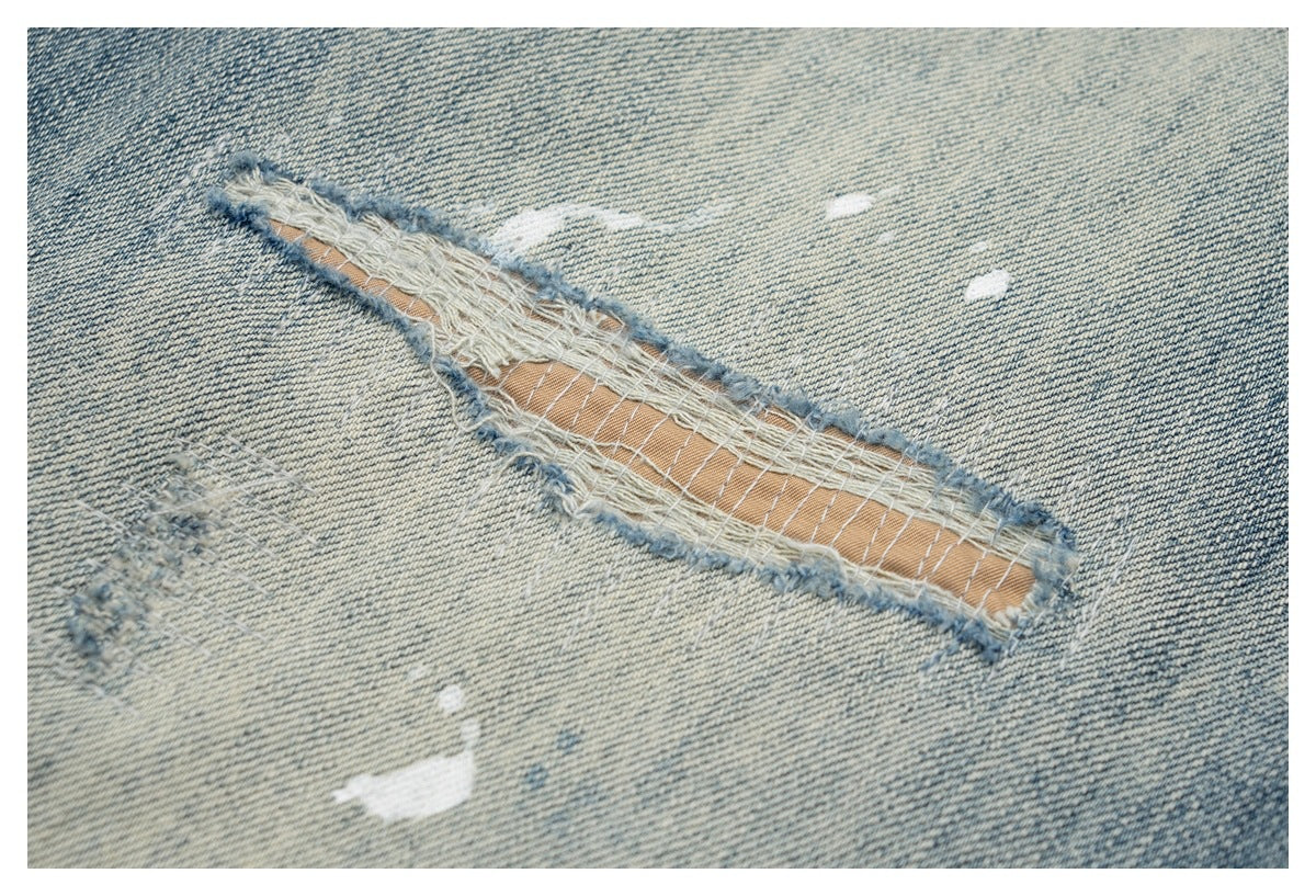 Close-up of a long distressed slit in pale blue denim, with frayed edges and exposed threads.