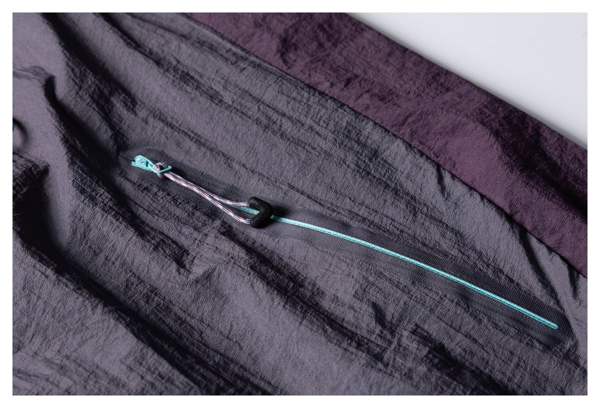 Close-up of a dark gray-purple jacket pocket with a turquoise zipper and cord pull.