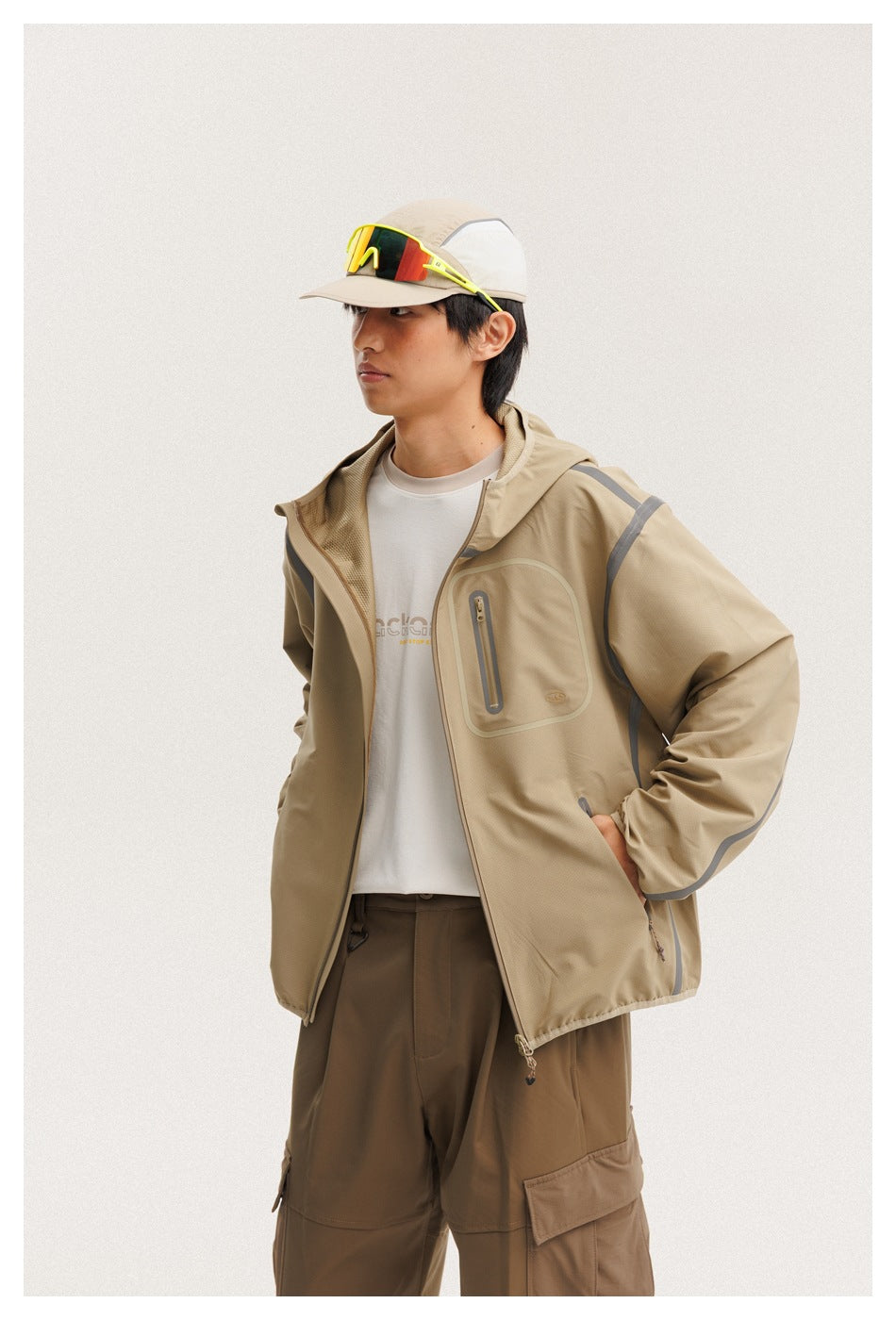 Close view of a model wearing an open tan hooded jacket with gray trim and a zip chest pocket.