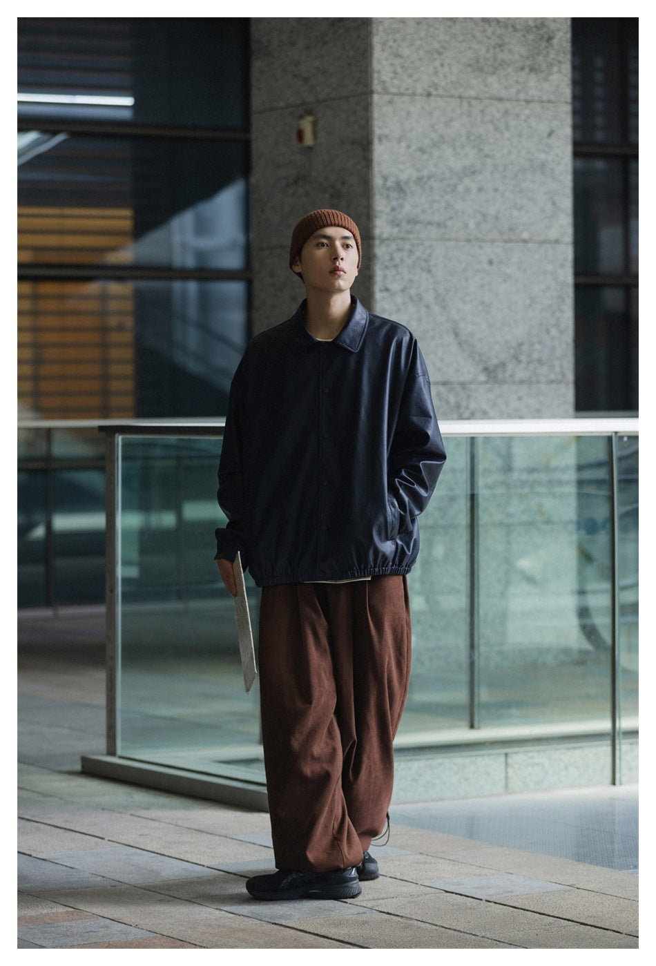 Full-length model wearing brown wide-leg trousers, a dark button-front jacket, and a rust beanie.