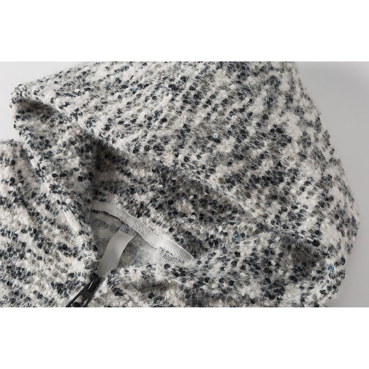 Close-up of a black-and-white fuzzy jacket fabric with the inner neck label and zipper visible.