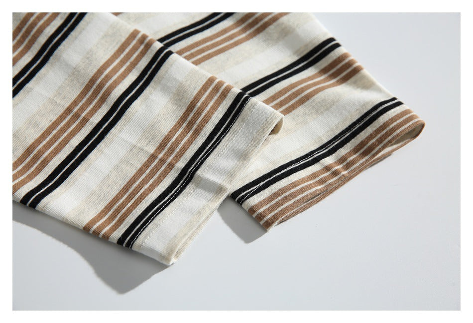 Close-up of a stitched hem on cream fabric with black and tan stripes, laid flat on a white surface.