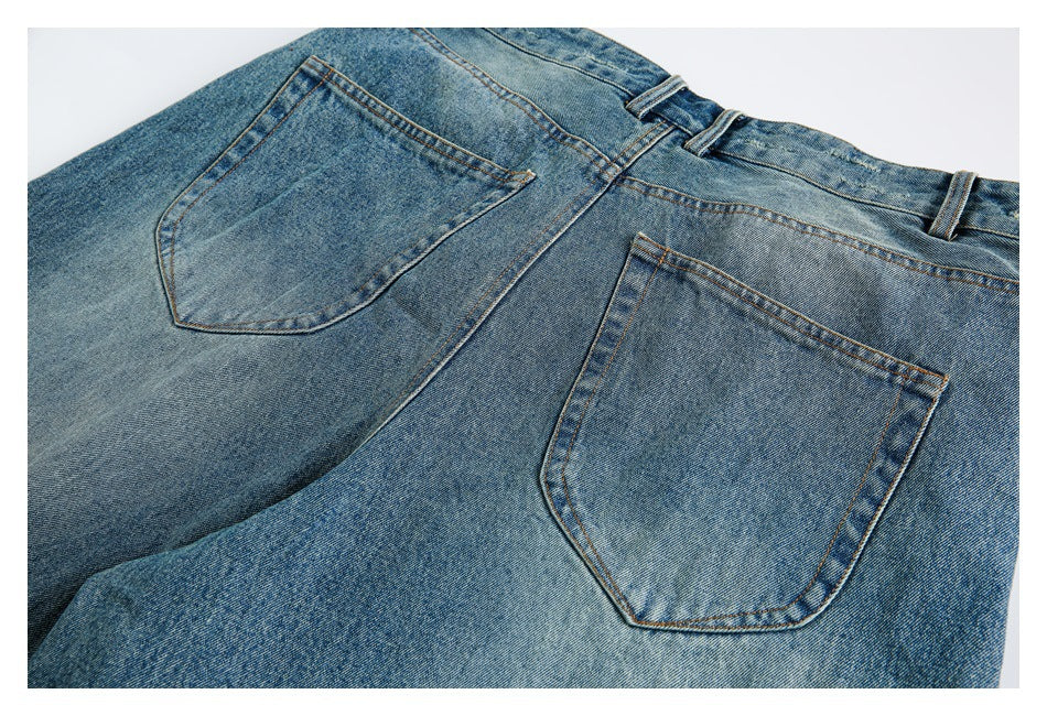 Back view of blue washed jeans laid flat, showing two patch pockets, belt loops and orange stitching.