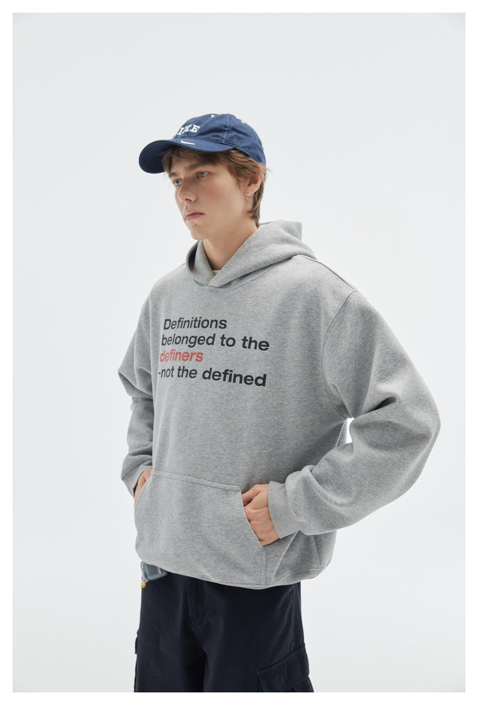 Model wearing a light gray text-print hoodie with a kangaroo pocket and dark pants, shown from the front.