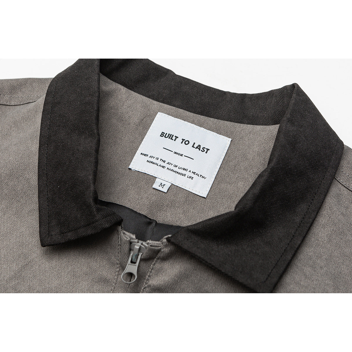 Close-up of a gray jacket’s dark collar, front zipper, and white neck label reading “BUILT TO LAST.”