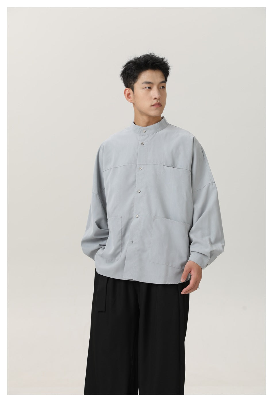 Model wearing a light gray oversized button shirt with a stand collar and two large front patch pockets, paired with black