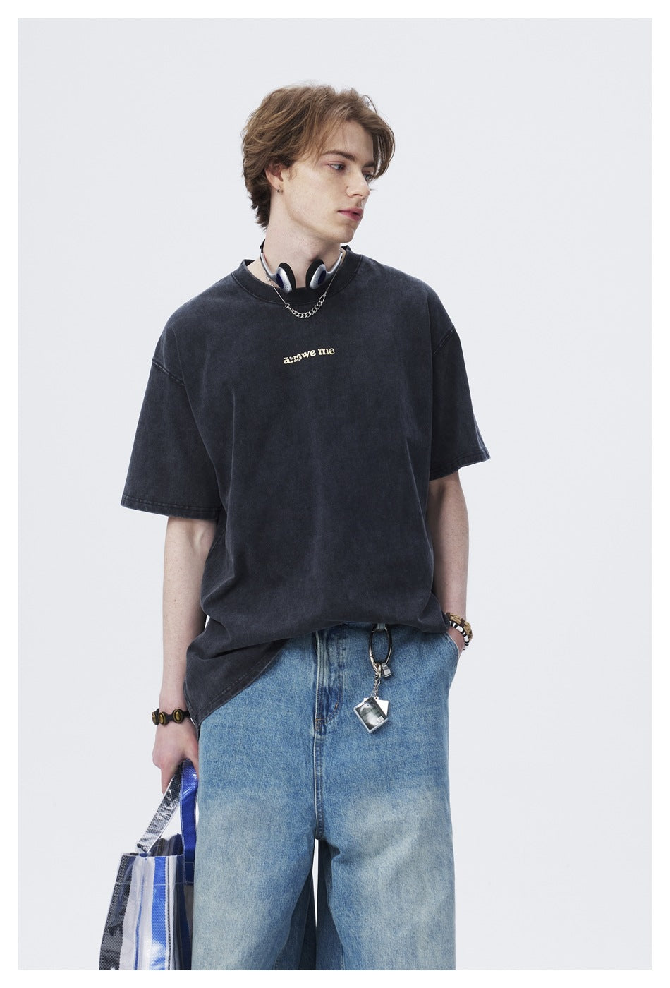 Waist-up view of a model wearing a dark oversized T-shirt with small light chest lettering and blue jeans.