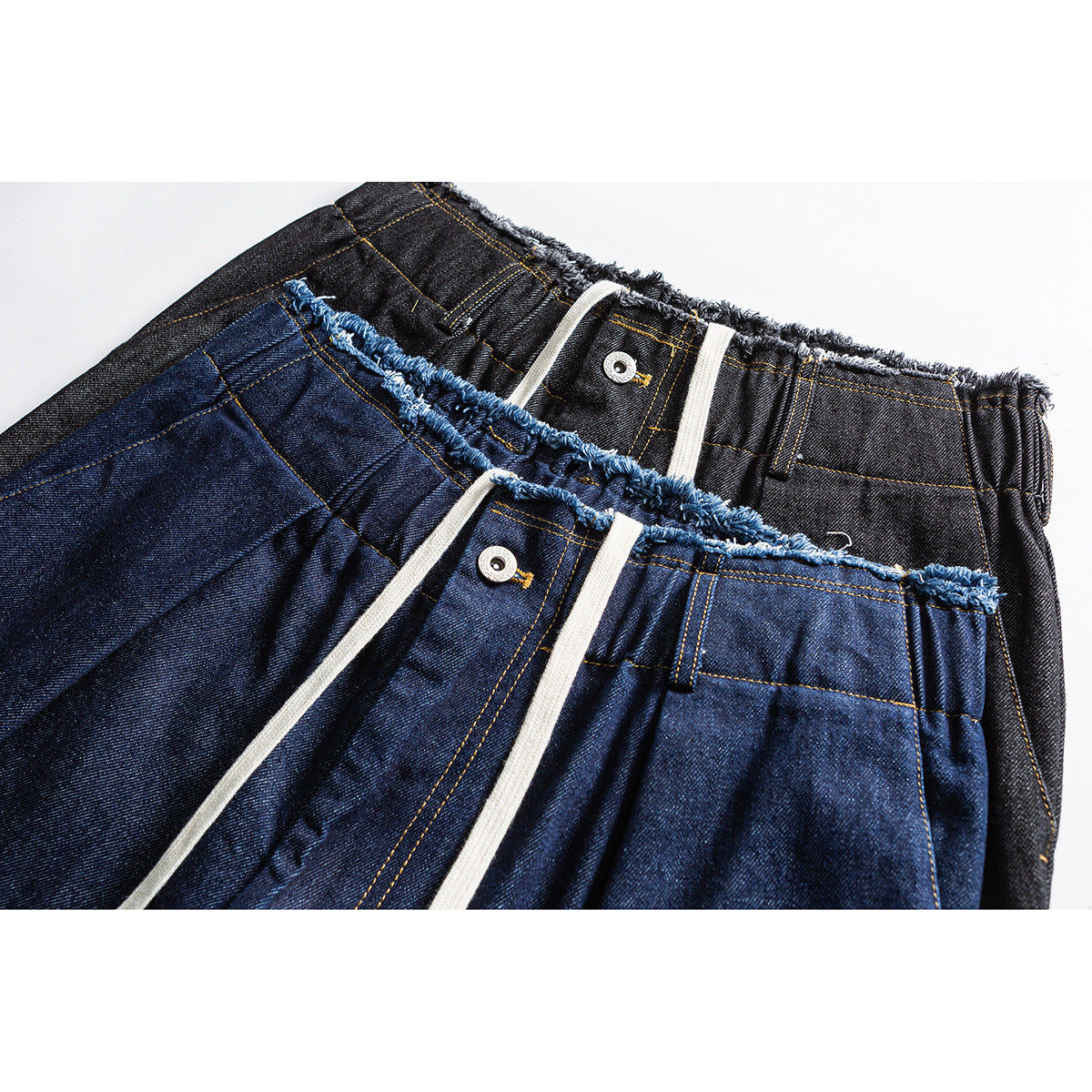 Close-up of blue and charcoal wide-leg jeans showing drawstrings, metal buttons, and frayed elastic waistbands.
