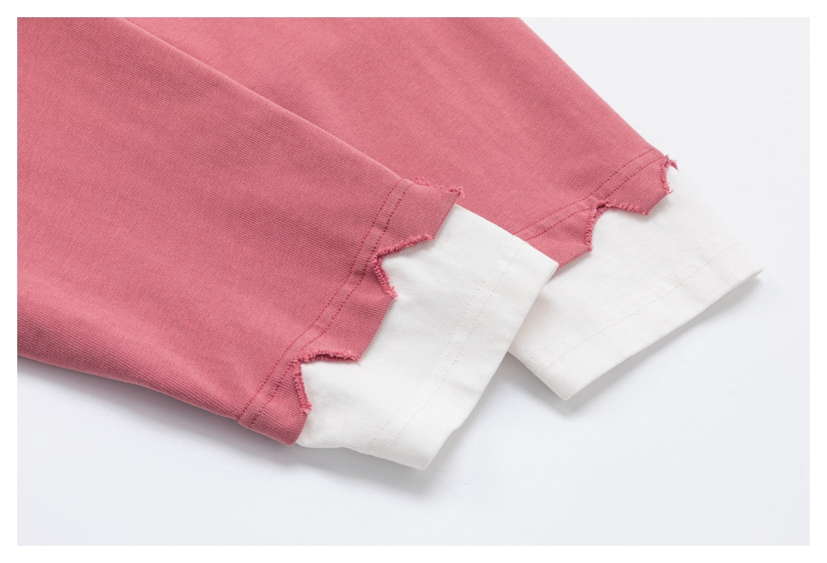 Close-up of dusty rose sweatshirt sleeve cuffs with irregular cut edges layered over white cuffs.