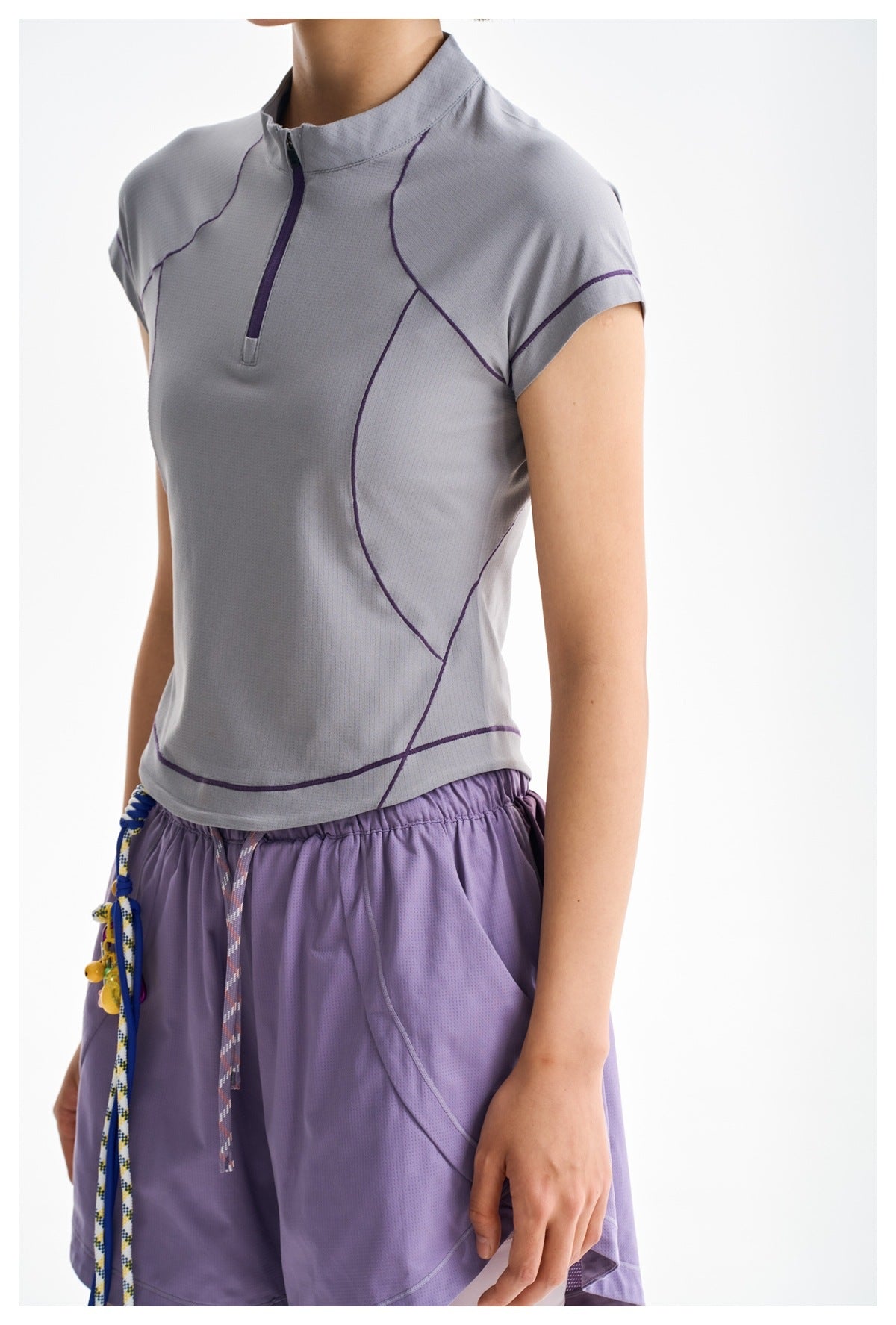 Close view of a model wearing a light gray-lilac zip-neck top with purple seam accents and lilac shorts.