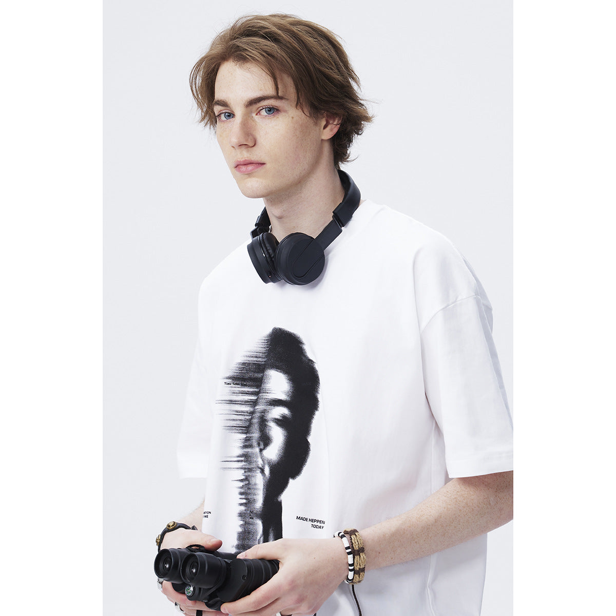 Close view of a model wearing a white short-sleeve T-shirt with a large black distorted portrait graphic.
